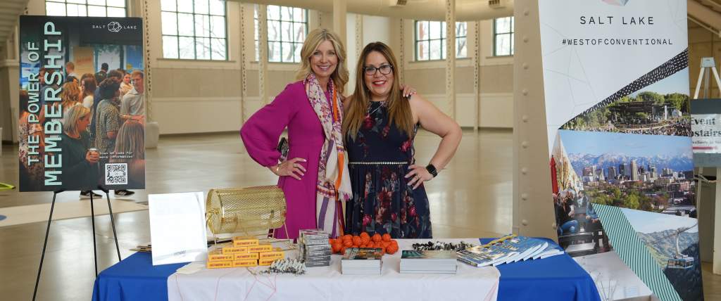 Kim Stowe and Cristina Chavez standing behind a table with a Visit Salt Lake logo drape and a sign that says The Power of Membership