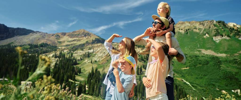 Family on a mountain trail all shading their eyes and looking at something in the distance with mountains in the background