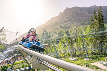 Woman looking like she is going fast around a corner on a single person coaster with sky and mountains around her