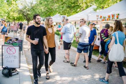 Couple strolling down the sidewalk in a crowd in front of several farmer's market booths
