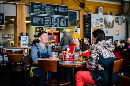 A group of people sitting at a table with food. The menu and serving counter are behind them