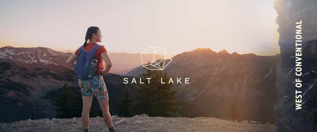 Person standing with backpack on in front of sunrise over mountain tops. On the right side of the image a vertical mountain range has West of Conventional on it